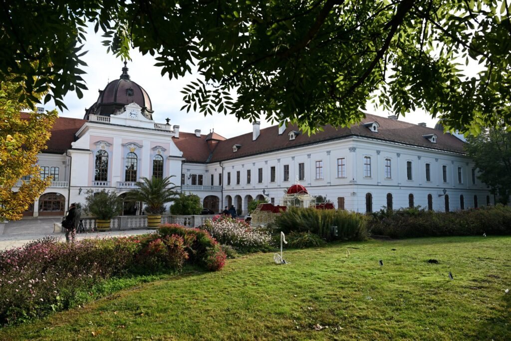 The white baroque Royal Palace of Gödöllő behind a garden with trees