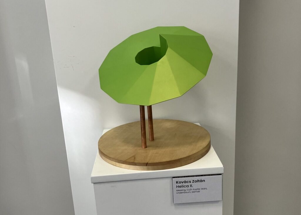 Green painted brass sculpture on two wooden rods over a round wooden base