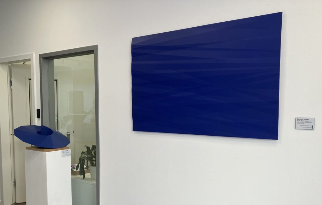 Blue powder-coated steel wall panel and a small blue sculpture on a plinth in the exhibition