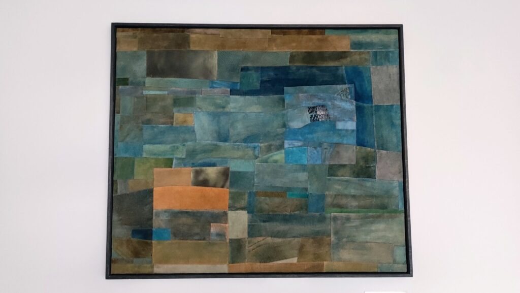 Textile artwork “Sea Eye” in blue and orange patches, framed on a white wall