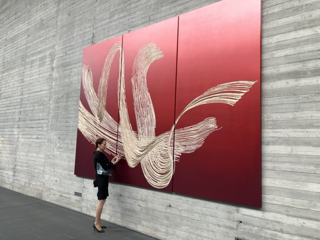 Large red wall artwork with cream brushstroke pattern by Wolfgang Flad, with a visitor beside it
