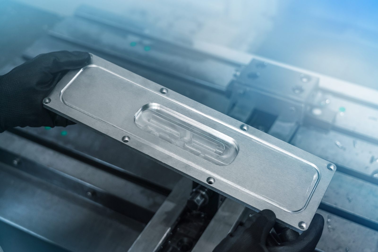 Sheet metal cover plate with an embossed pattern and screw holes, held in gloved hands